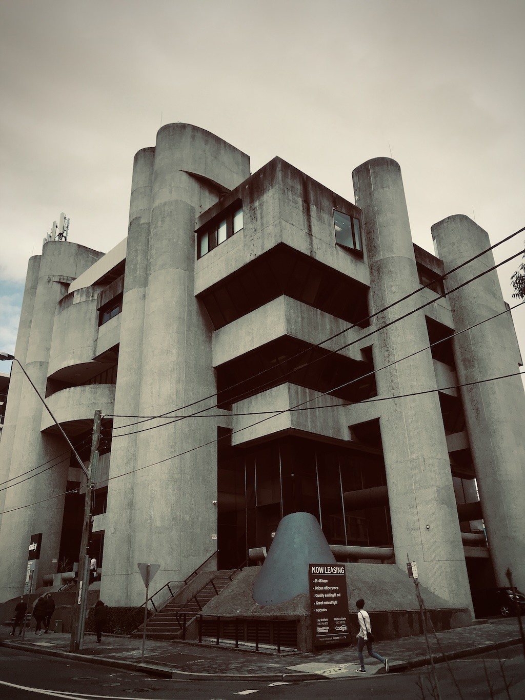 A brutalist concrete office building with cylindrical towers and a "Now Leasing" sign