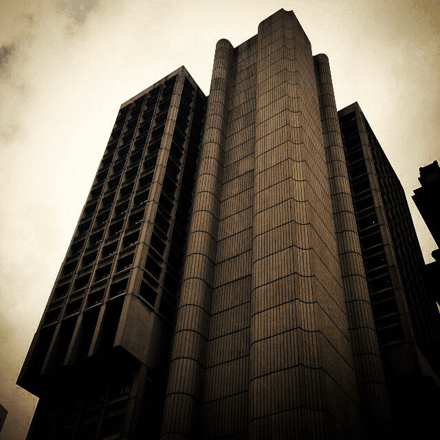 A dramatic low-angle photo of a brutalist high-rise tower against a bright sky