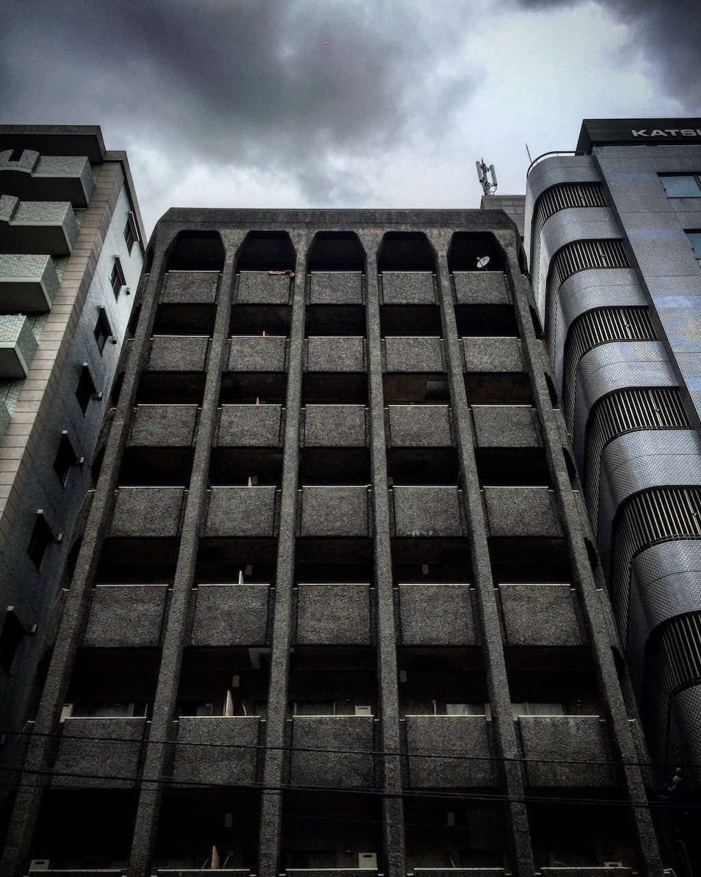 A brutalist apartment building with a grid of balconies, photographed from below under a stormy sky