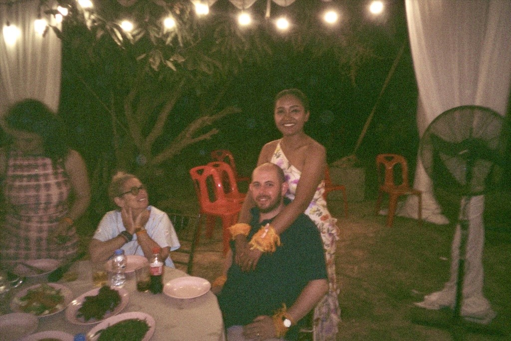Friends smiling around an outdoor dinner table at night, lit by string lights